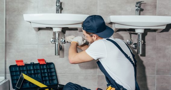 back view of young professional plumber fixing sink in bathroom